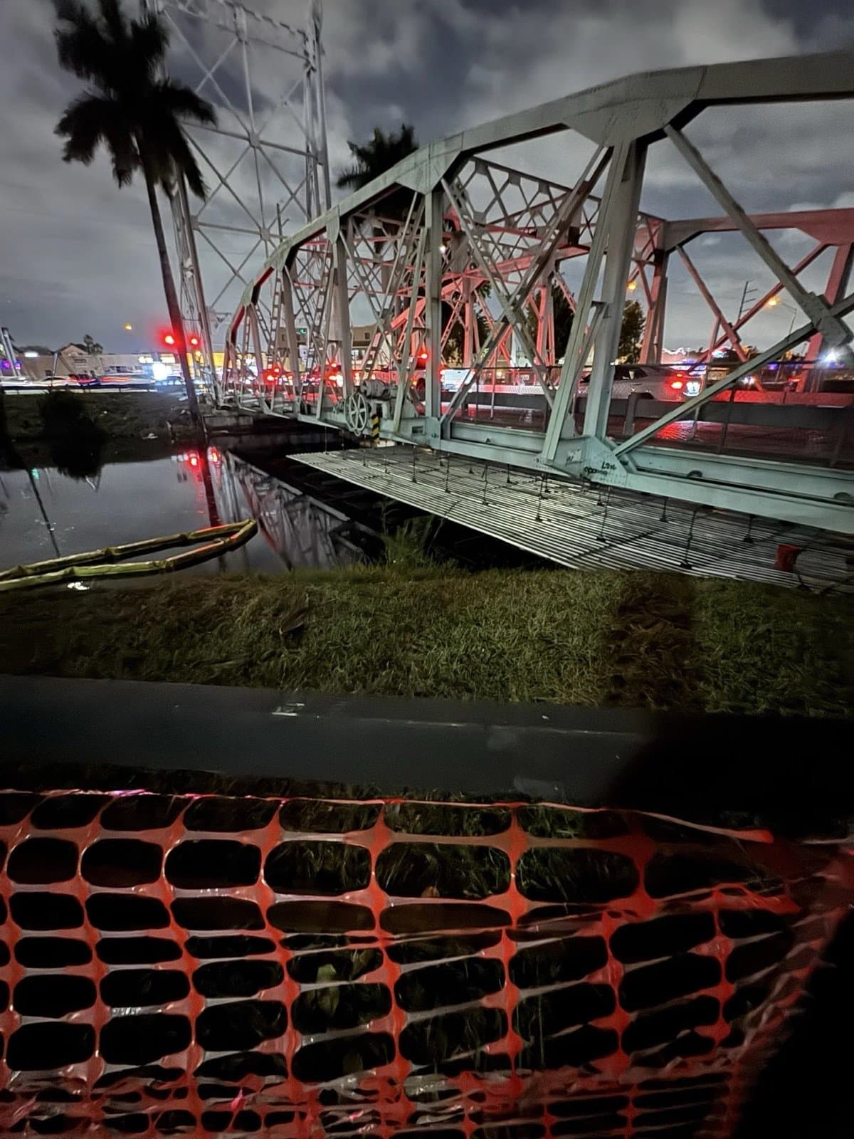 Truss swing bridge lit at night with traffic passing behind containment
