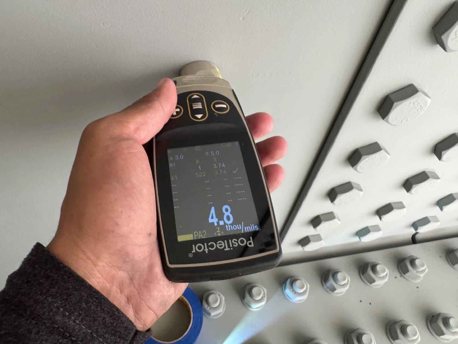 Dry film thickness gauge reading 4.8 mils on a coated bolt pattern