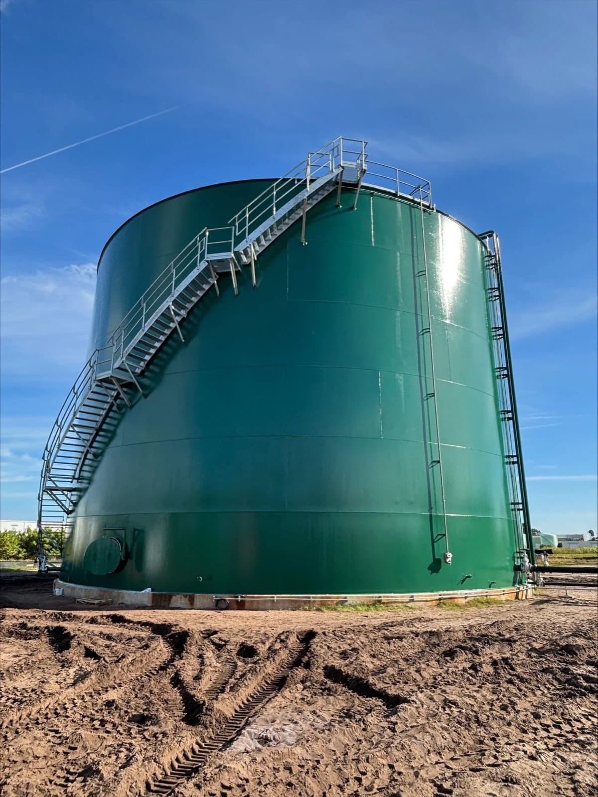 Freshly coated green storage tank with exterior stair against a blue sky